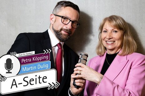 Petra Köpping und Martin Duloig stehen vor einer grauen Wand und halten ein Mikro in der Hand. Daneben die Aufschrift »Zwei für Sachsen. Podcast. Die A-Seite«