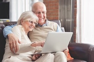 Ein älteres Pärchen sitz zusammen auf einem Sofa und beide schauen in einen Laptop